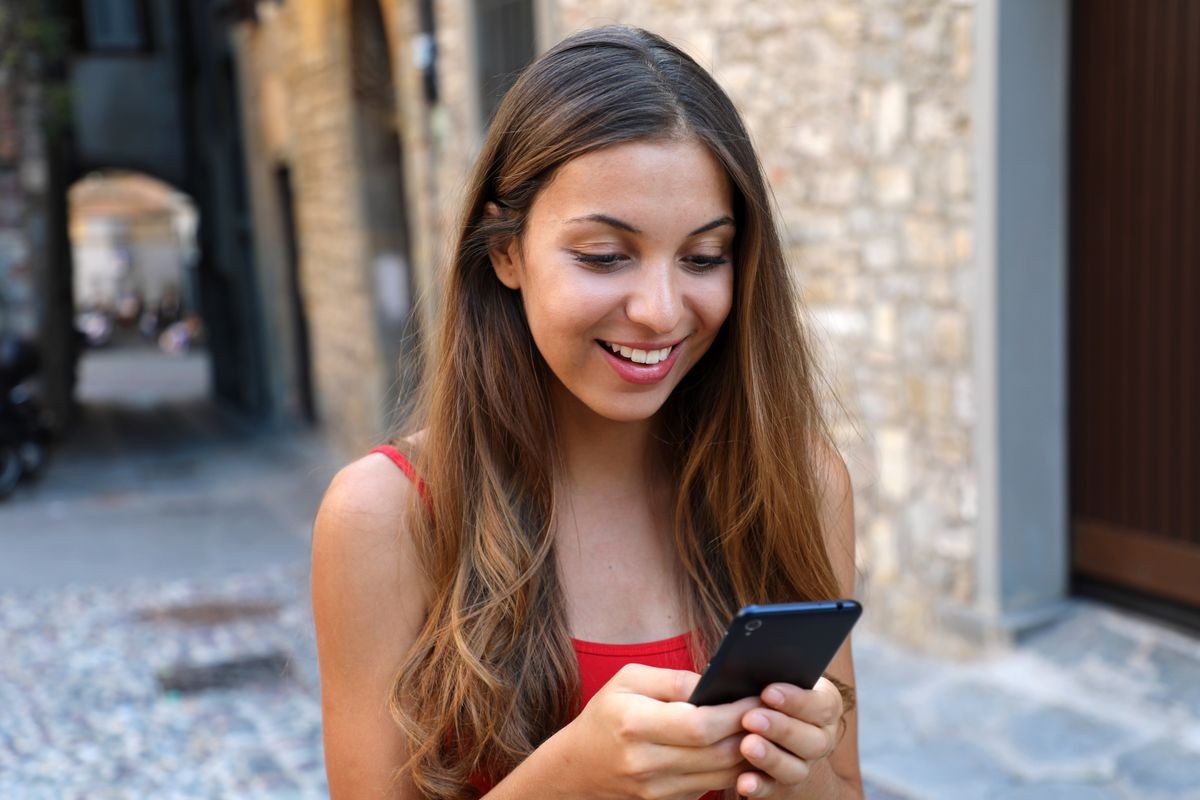 Smiling woman using mobile phone app to play video games online. City woman relaxing. Urban lifestyle background.